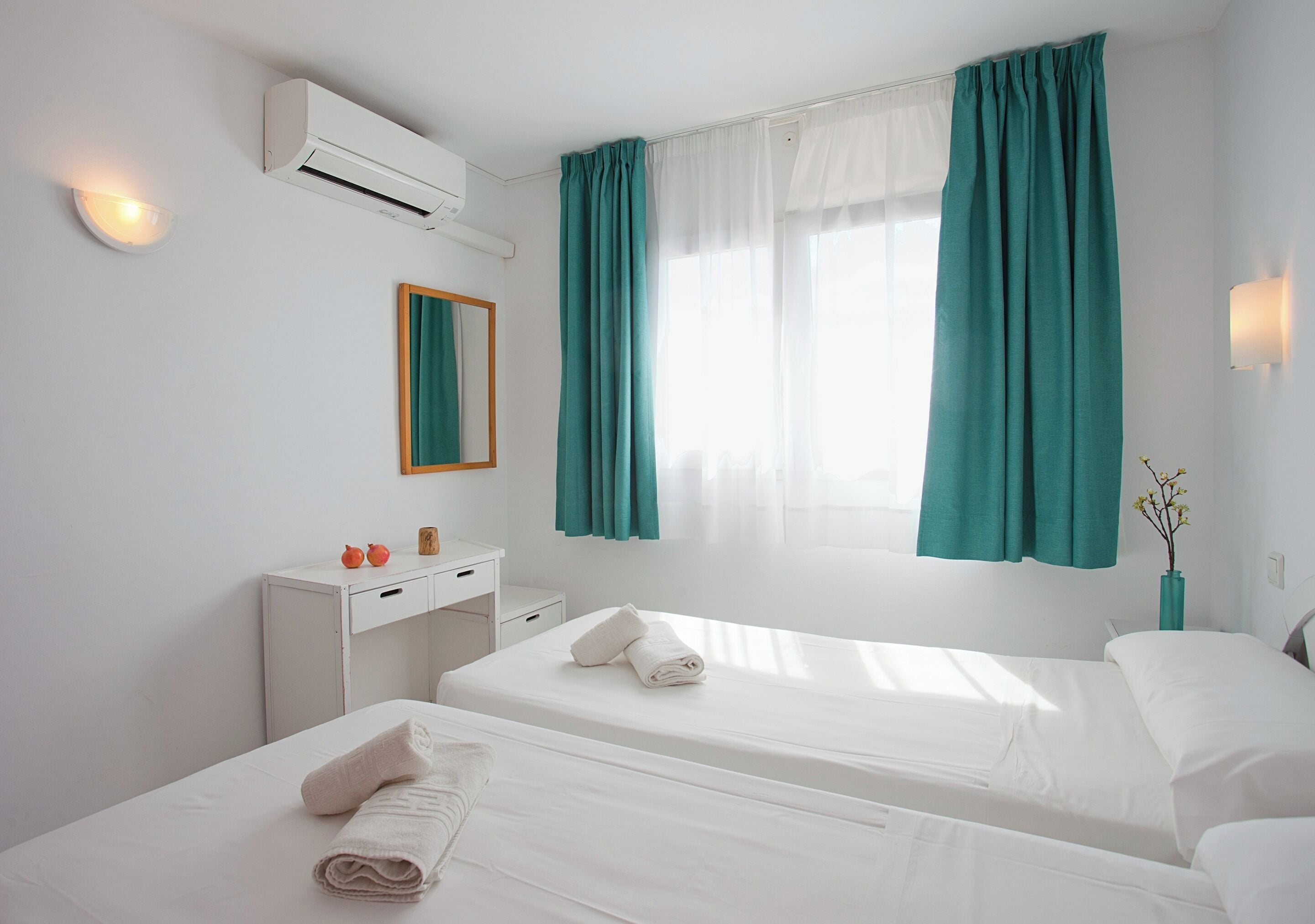 A hotel room with two beds, a desk, a mirror, and a window with curtains.