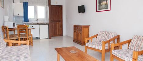 A living room with a sofa, two armchairs, a wooden coffee table, and a kitchen in the background.