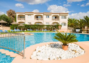 A hotel with a swimming pool, lounge chairs, and a palm tree. - Apartamentos Sol Romántica by DOT Suites (Manacor)