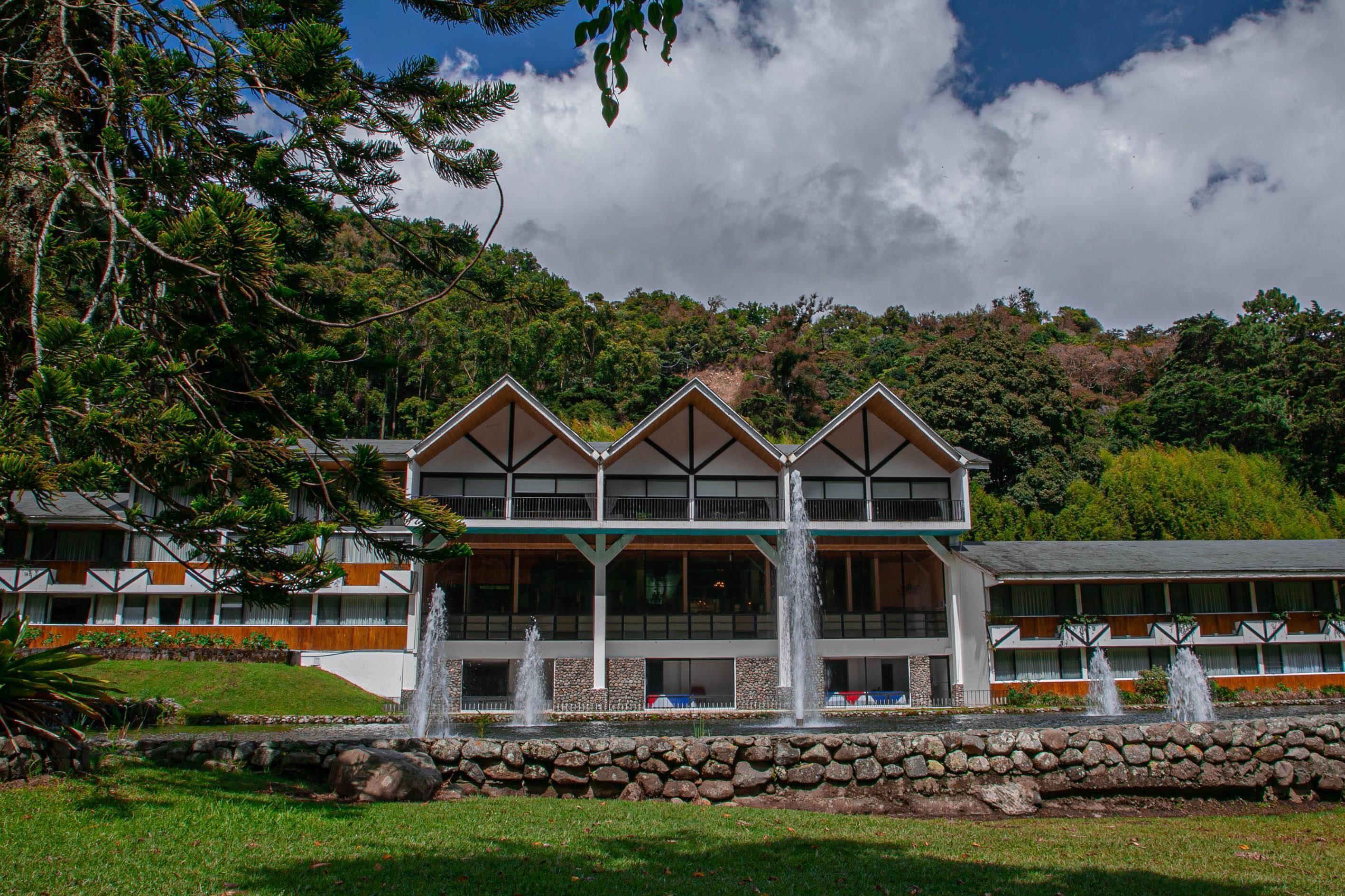 A hotel with a modern architectural design, featuring a prominent balcony and multiple water fountains in the courtyard.