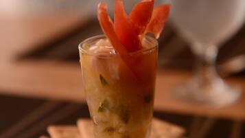 A glass of cocktail with a lime wedge and carrot garnish on a white plate, accompanied by crackers and a fork.