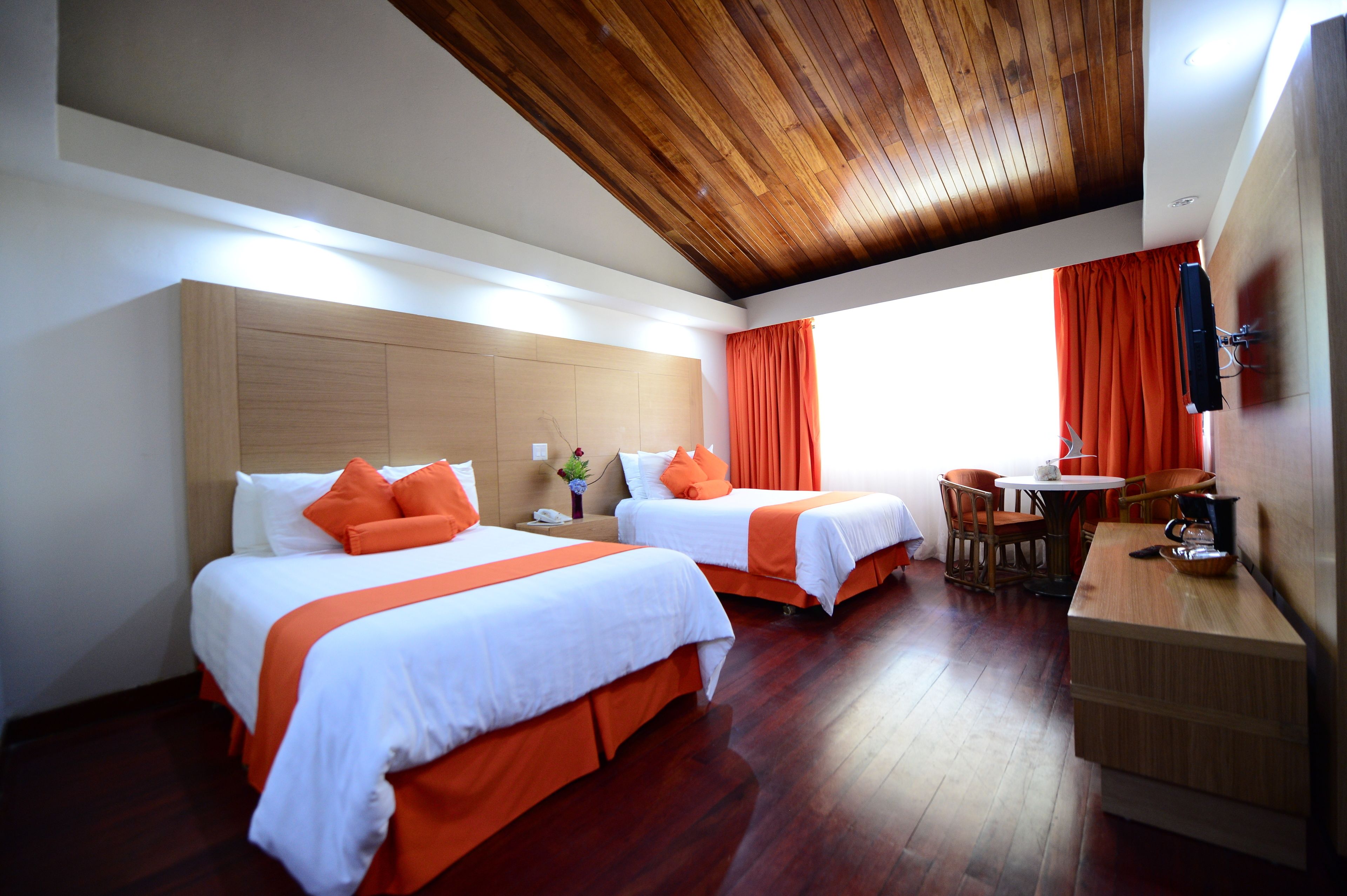 A hotel room with two beds, wooden ceiling, and a small dining area with a table and chairs.