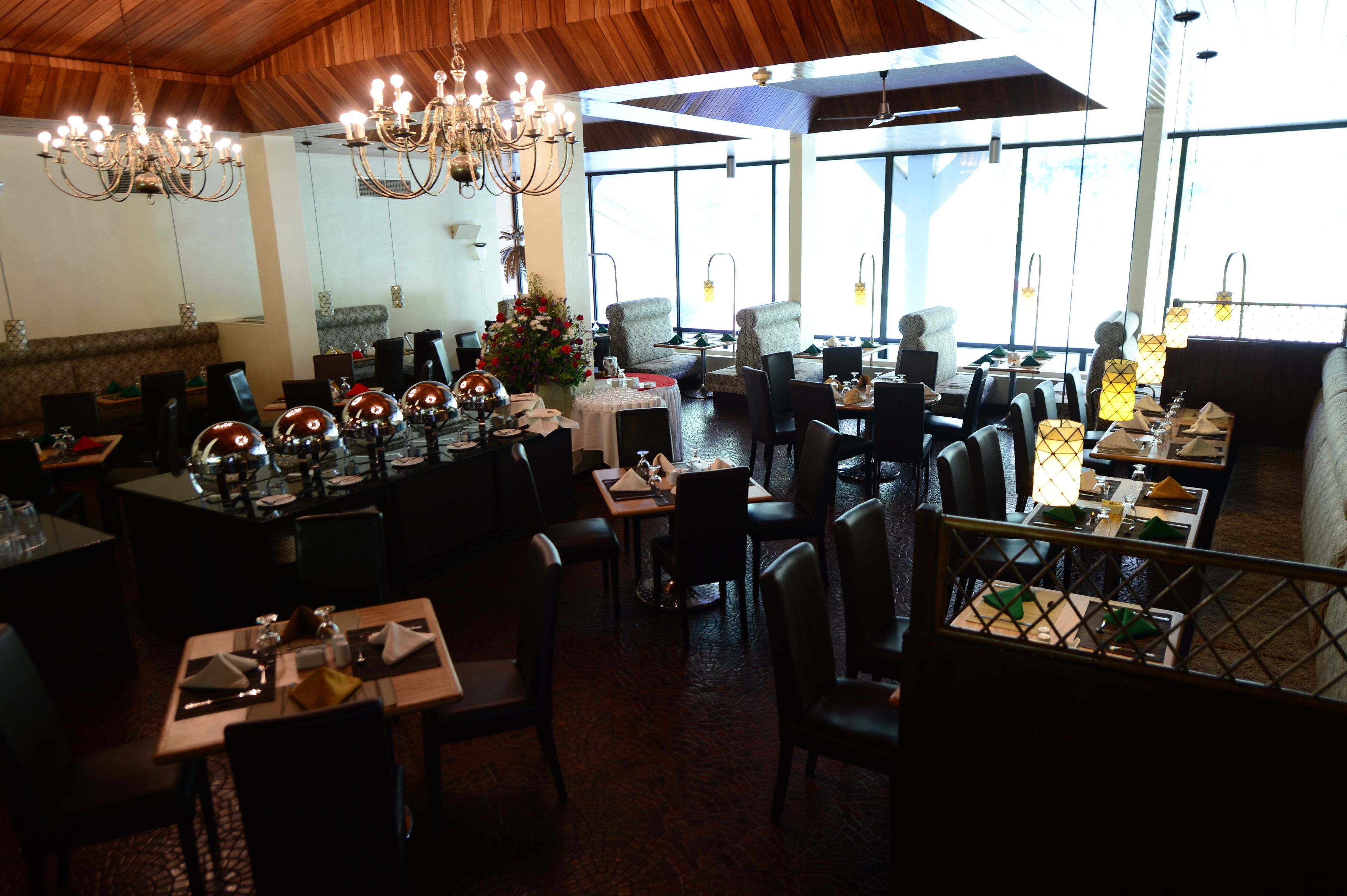 Un restaurante con varias mesas y sillas, candelabros y amplios ventanales que dejan entrar luz natural.