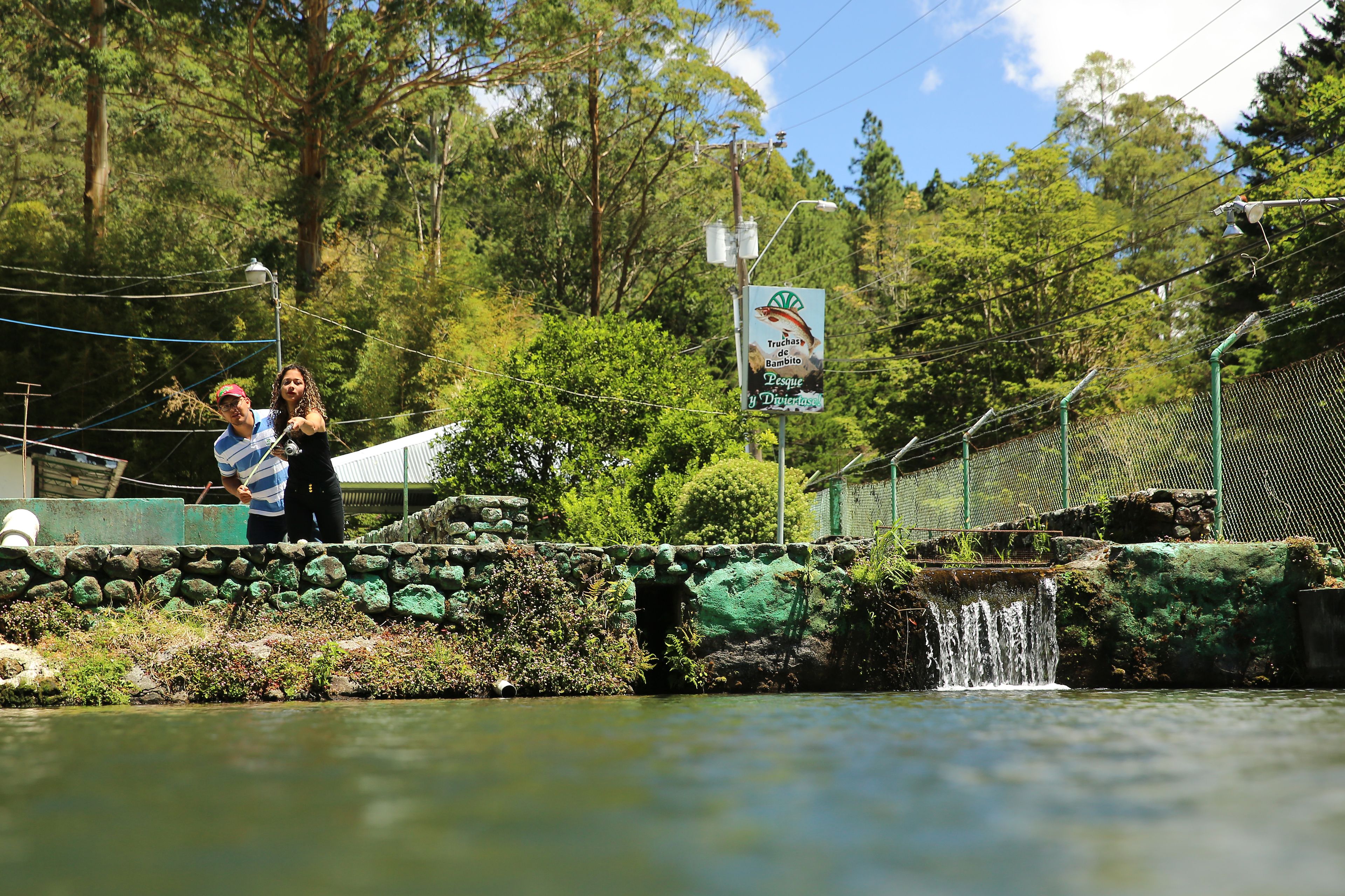 Un puente de piedra sobre un arroyo pequeño, con un letrero que indica una zona de pesca de truchas.