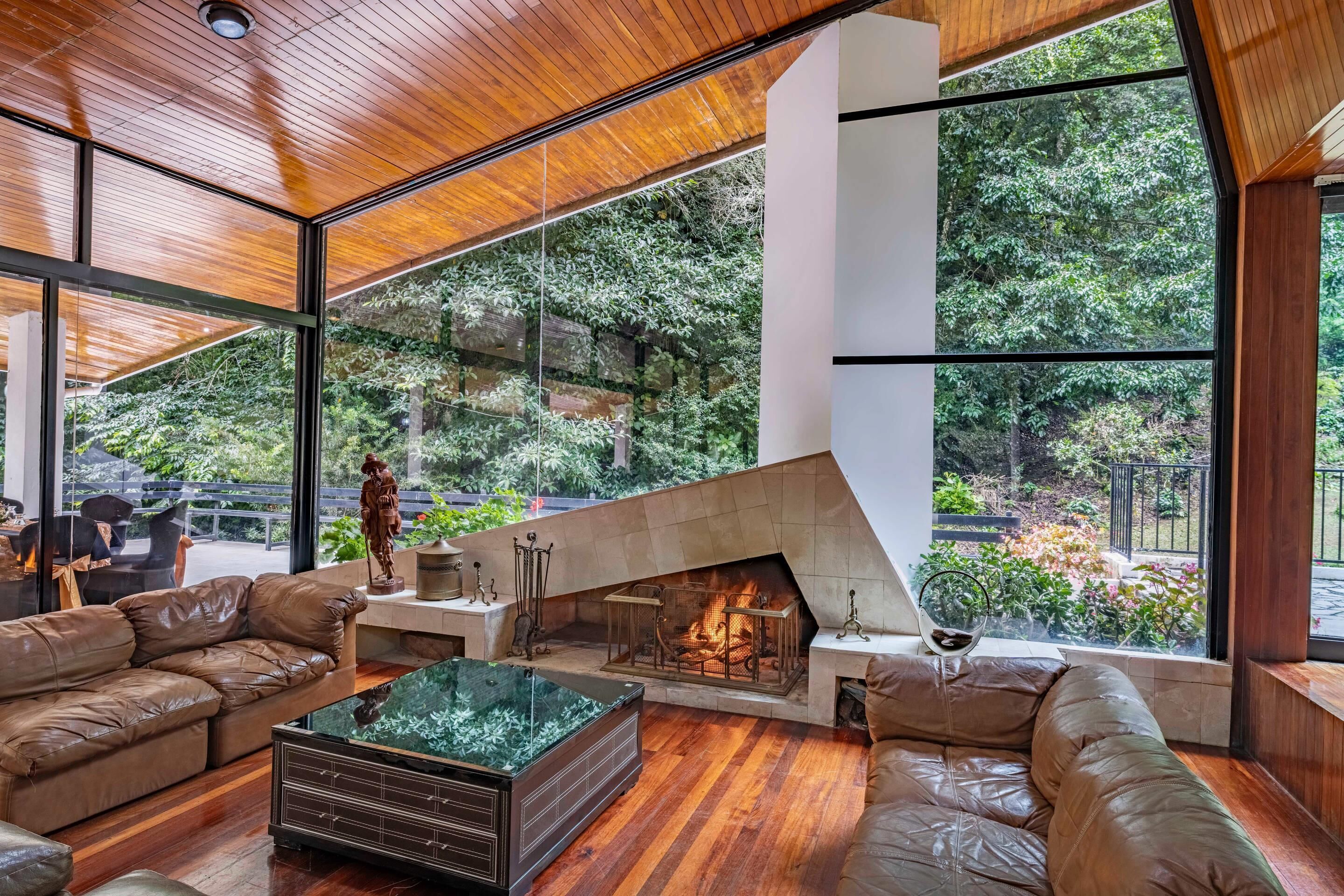 A modern interior with a fireplace, leather sofas, and large windows offering a view of the outdoors.