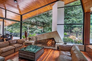 Un intérieur moderne avec une cheminée, des canapés en cuir et de grandes fenêtres donnant sur l’extérieur.