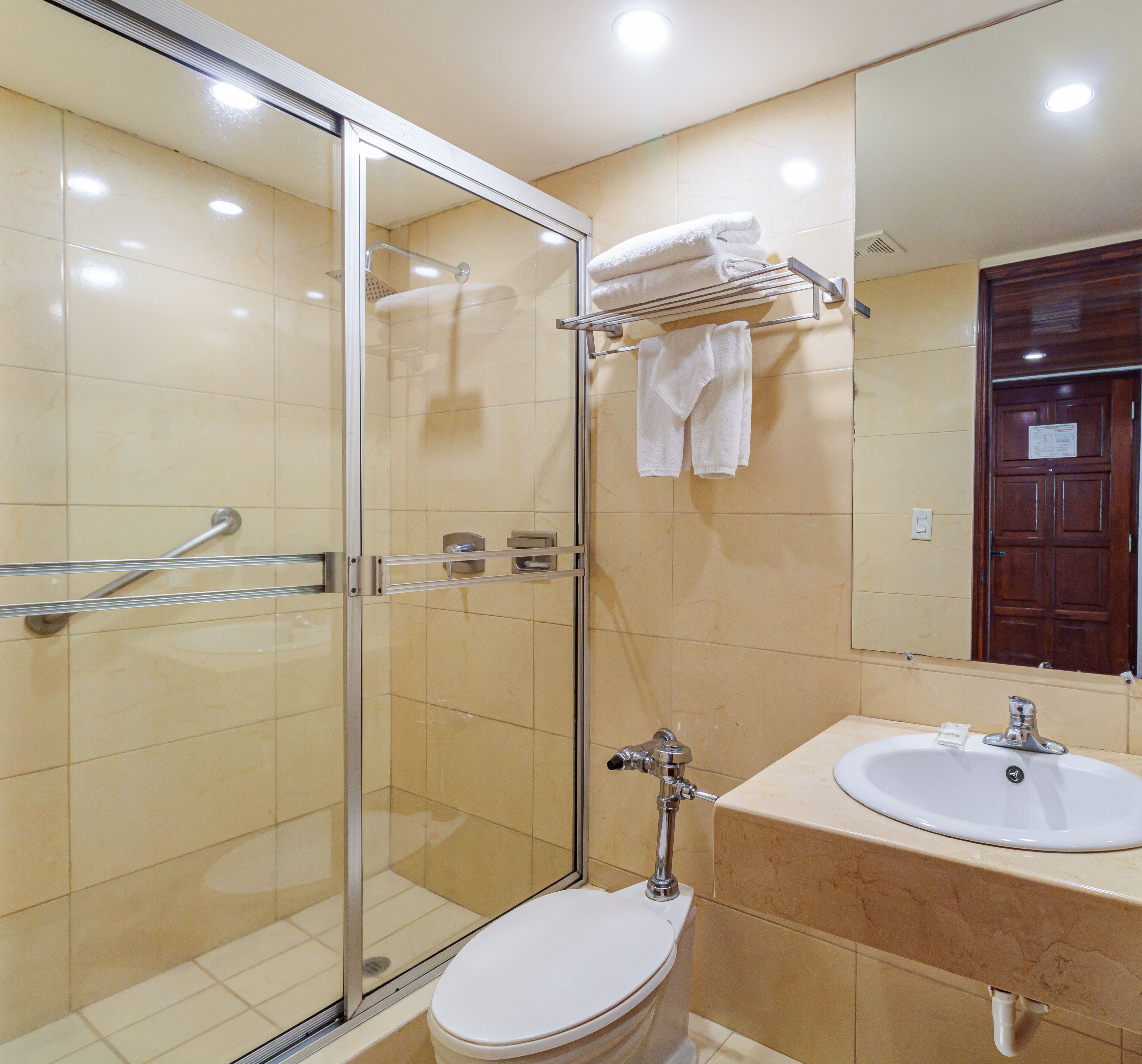 Un baño moderno con cabina de ducha de vidrio, inodoro blanco y lavamanos con espejo superior.