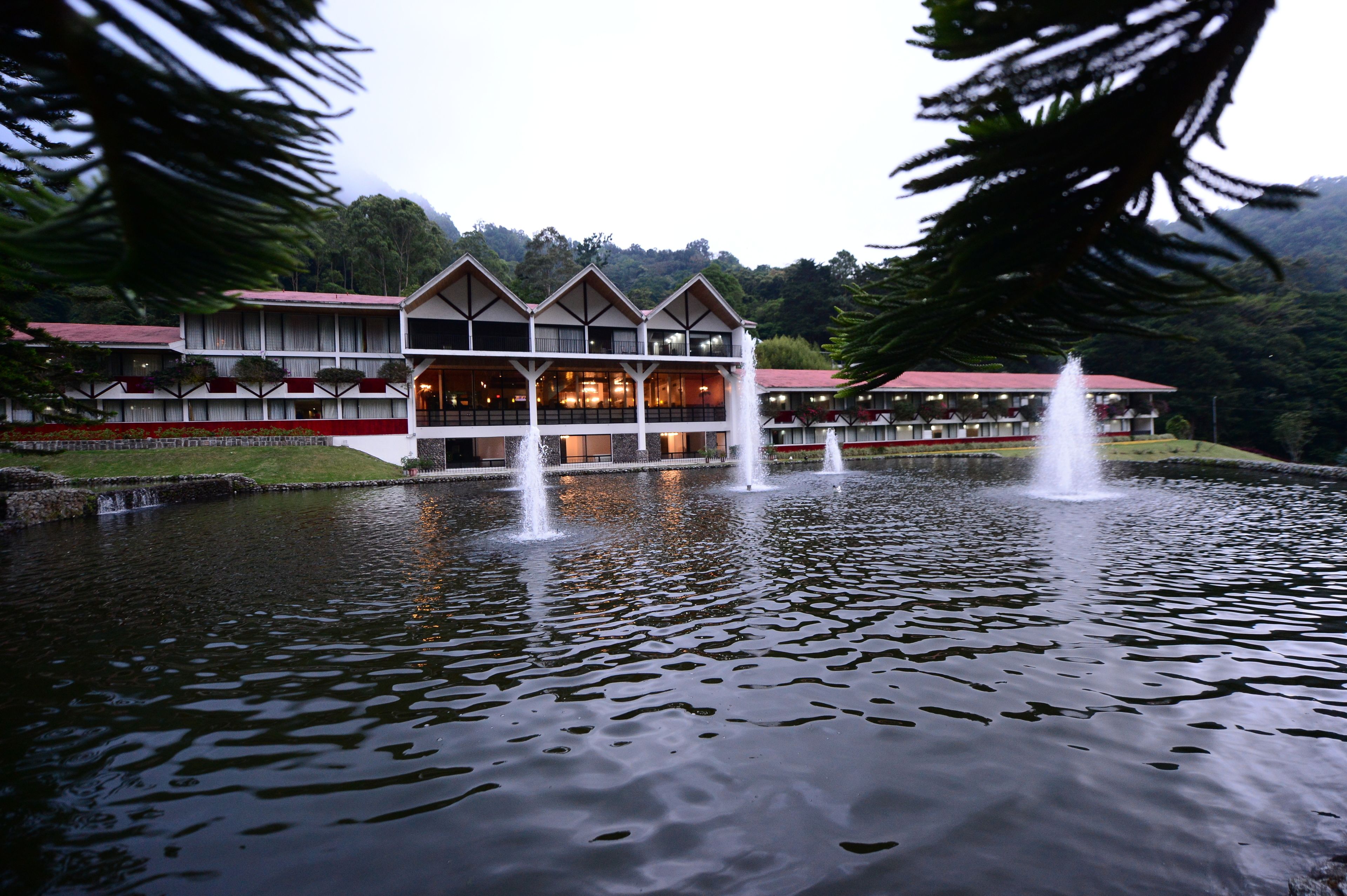 A hotel with a large water fountain in front, surrounded by a well-maintained lawn and trees.