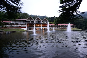 A hotel with a large water fountain in front, surrounded by a well-maintained lawn and trees.
