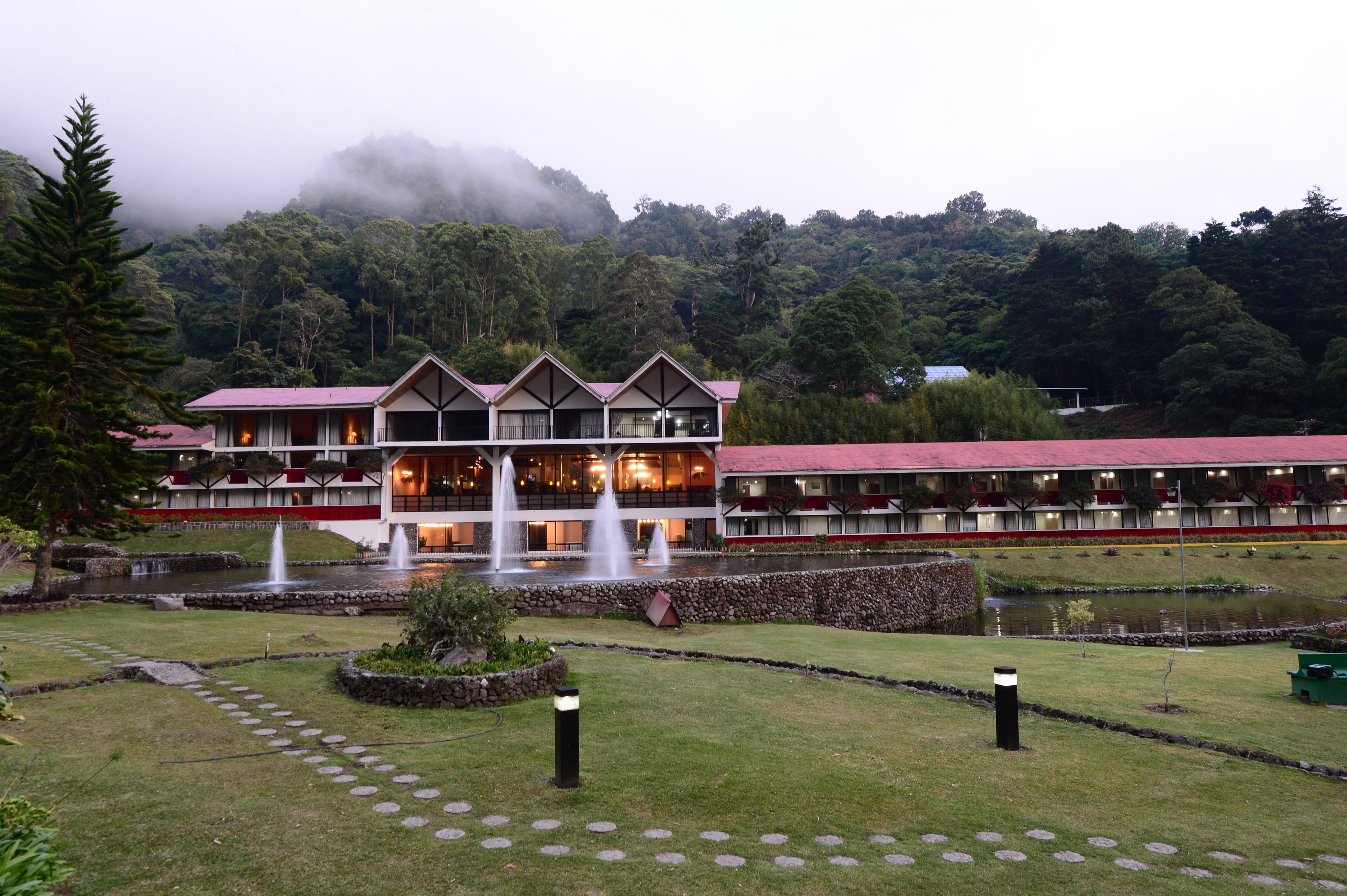 A hotel with a central courtyard, multiple fountains, and a view of a forested mountain.