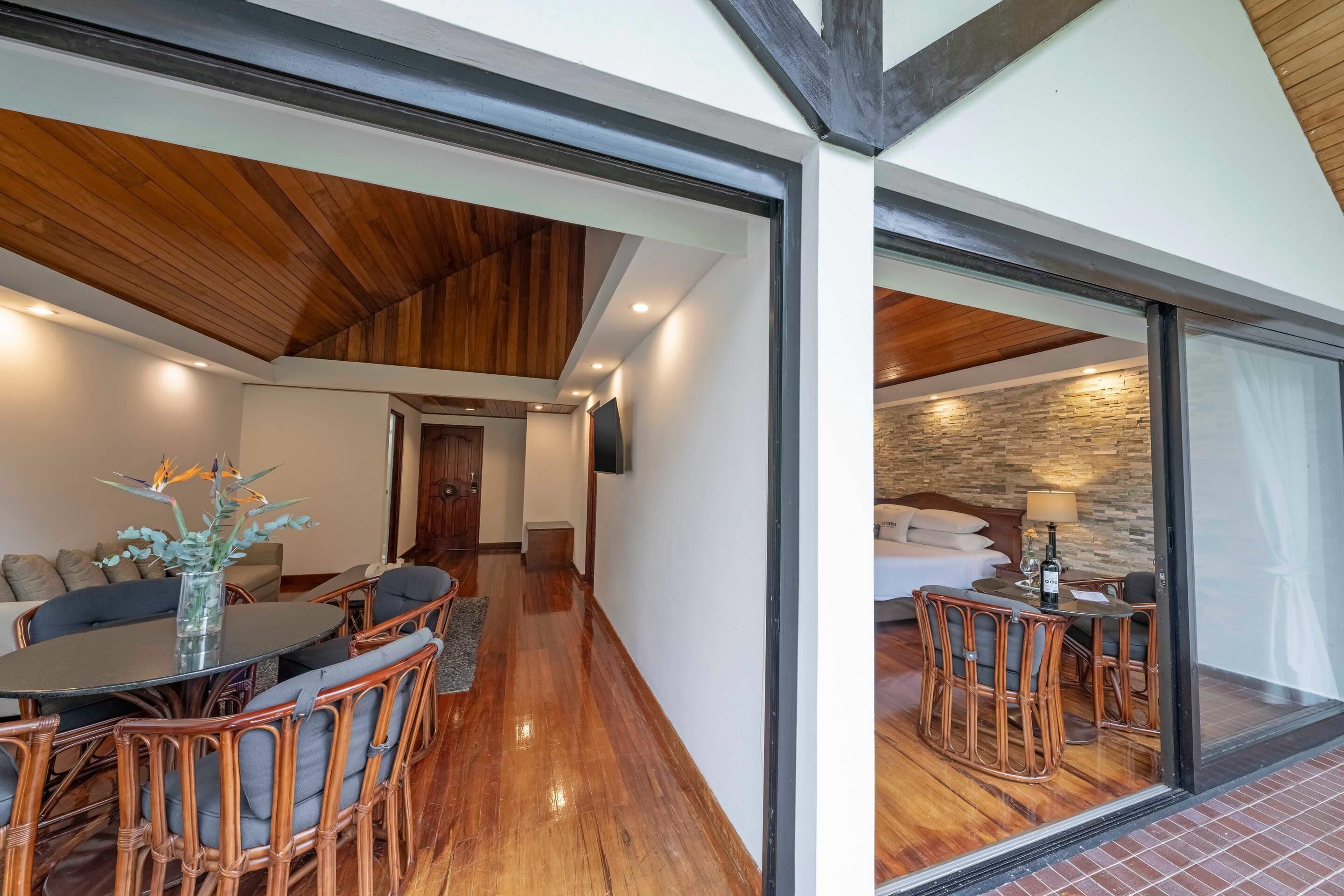 Una habitación de hotel moderna con zona de comedor, techo de madera y pared de piedra.