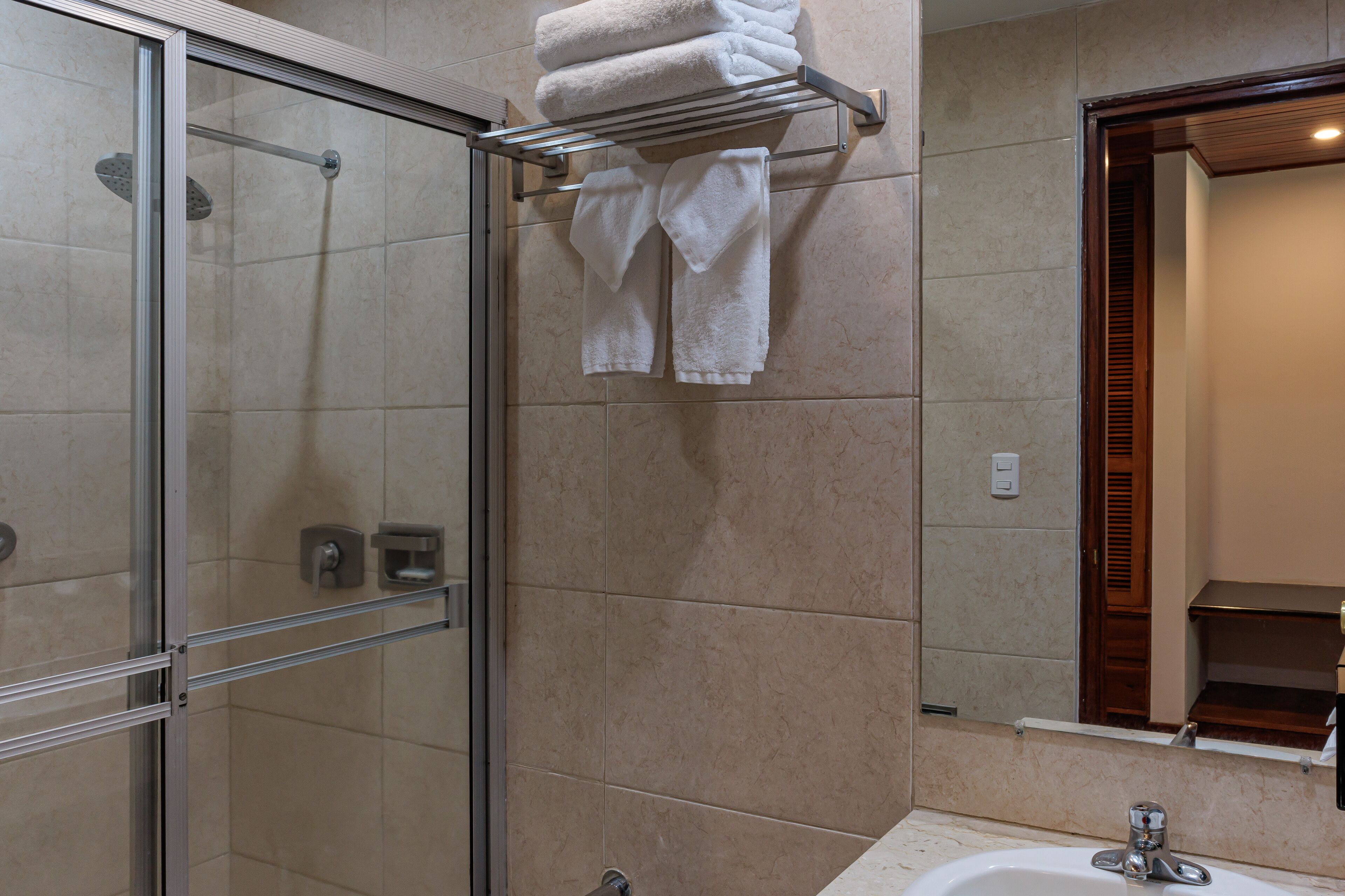 A bathroom with a glass shower enclosure, a towel rack with folded towels, and a sink with a mirror.