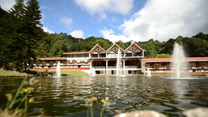 Un hotel con techo rojo, varios pisos y una fuente al frente.