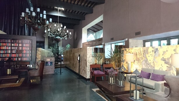 A lobby with a chandelier, bookshelves, a reception desk, and seating areas. - Hotel Gobernador (Durango)
