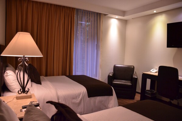 A hotel room with two beds, a desk with a lamp, a chair, a TV, and a window with curtains. - Hotel Gobernador (Durango)