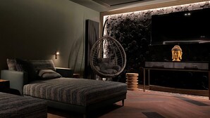 A modern bedroom with a large bed, a hanging chair, a TV, and a Buddha statue. - The Gailes Hotel and Spa (Irvine)