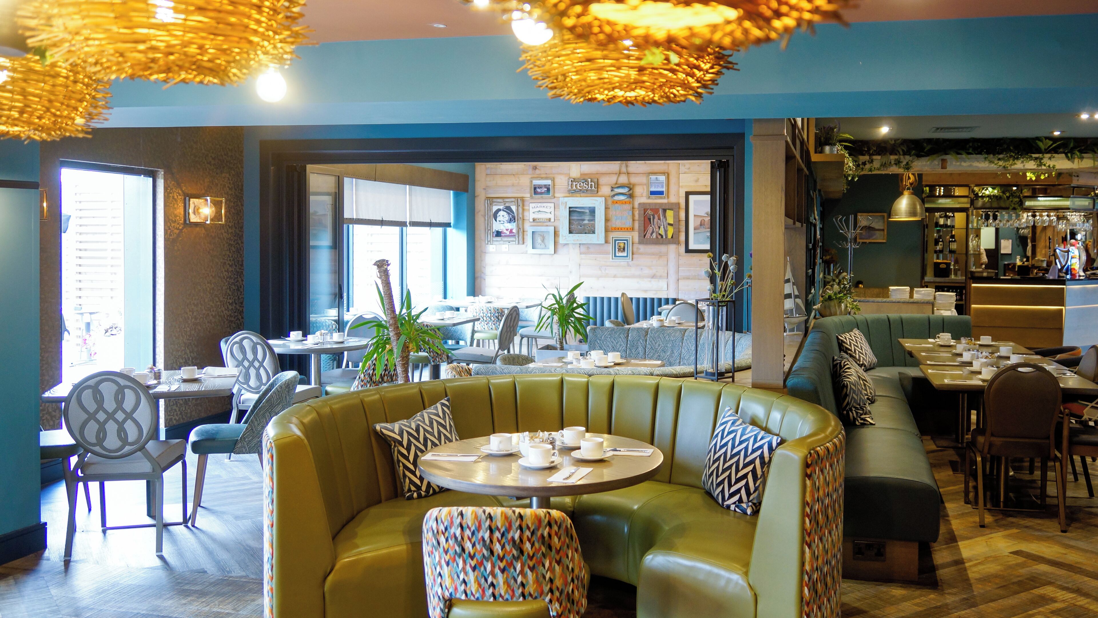 A restaurant with green upholstered seating, tables with white tableware, and a bar area with shelves of bottles.