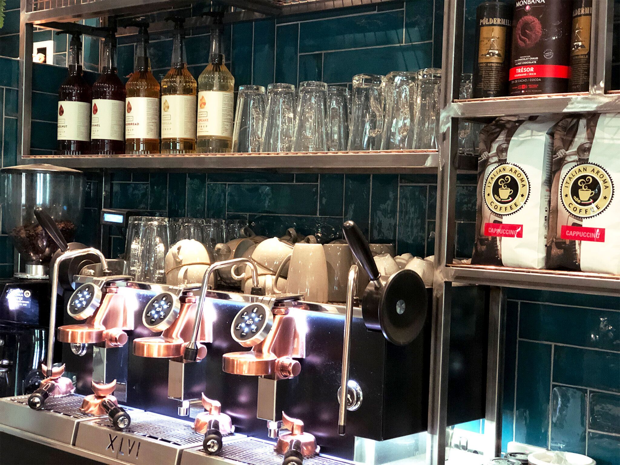 Une machine à café dotée de plusieurs postes de préparation, une sélection de grains de café et une variété de verres exposés.