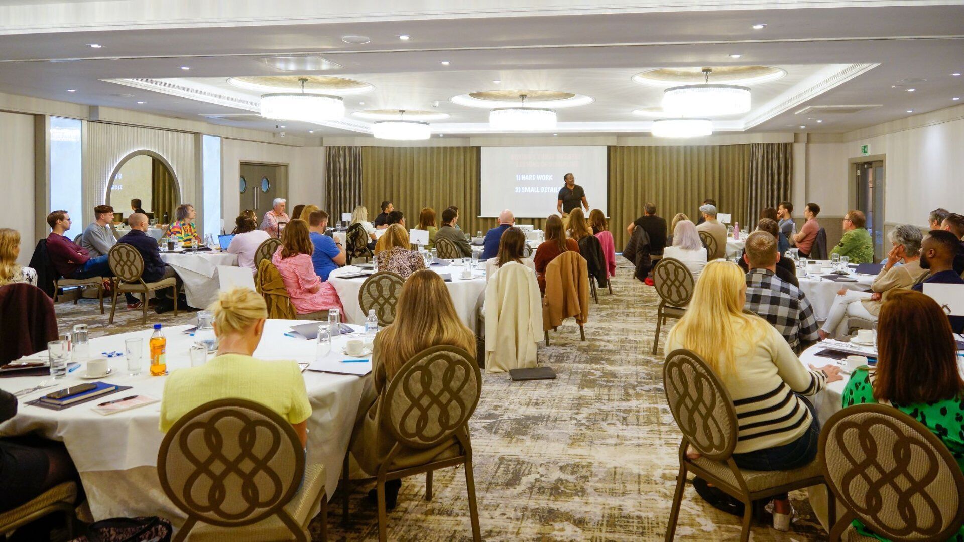 A conference room with round tables, chairs, and a presentation screen.