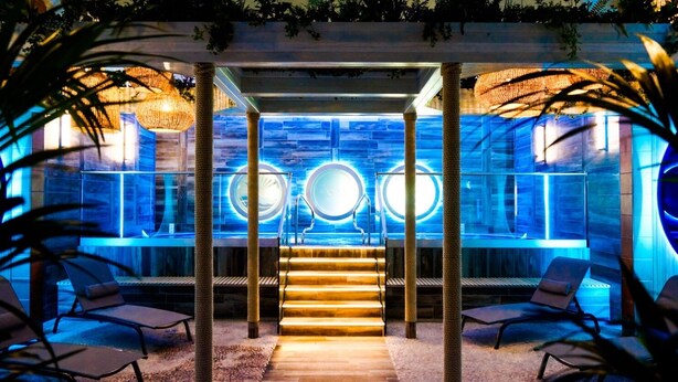 A modern spa area with a stone wall, a staircase, and lounge chairs. - The Gailes Hotel and Spa (Irvine)