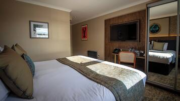A hotel room with a large bed, a desk with a chair, a television, and a mirror.