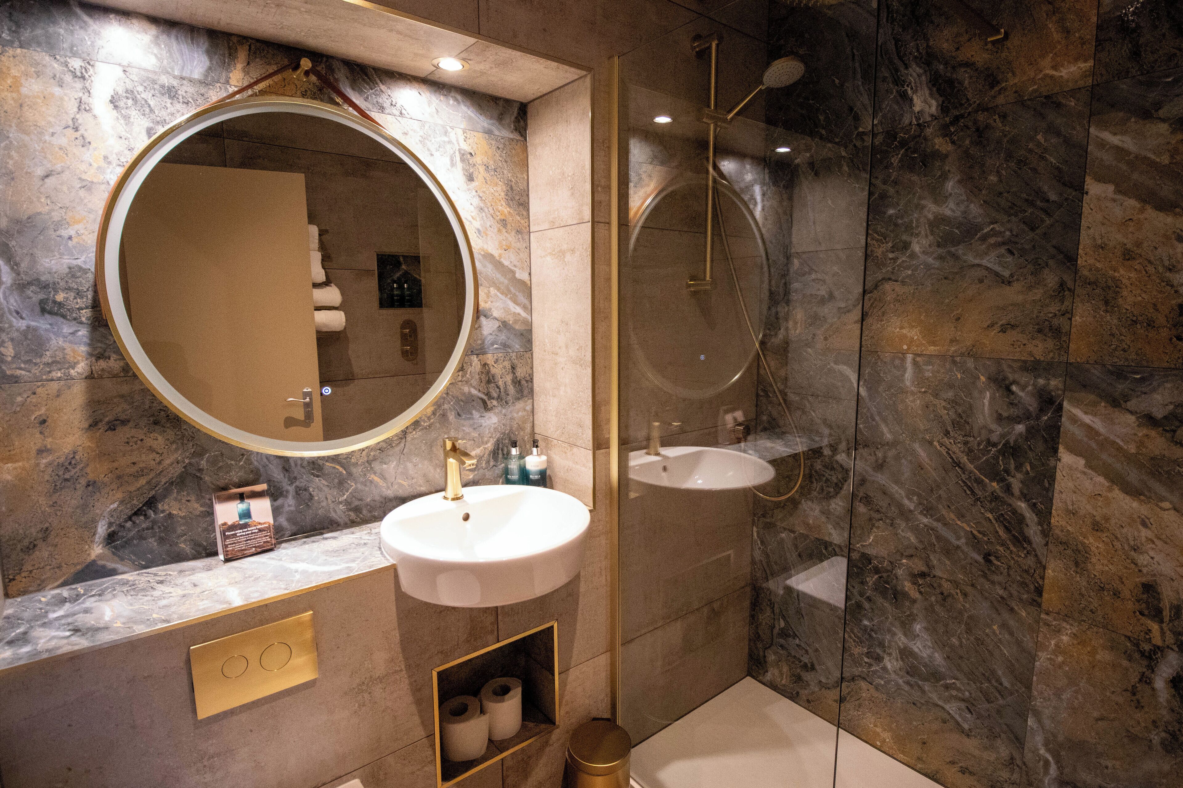 A modern bathroom with a round mirror, a sink, and a shower.