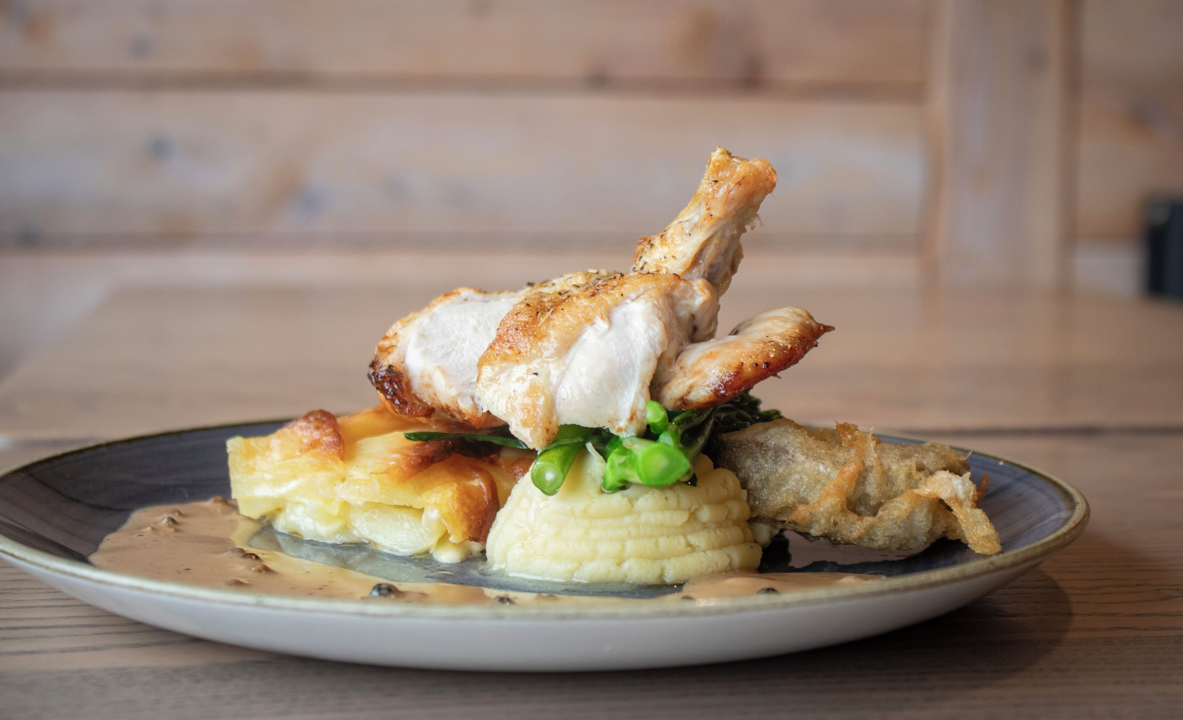 A plate with a piece of grilled chicken, mashed potatoes, and corn on a wooden table.
