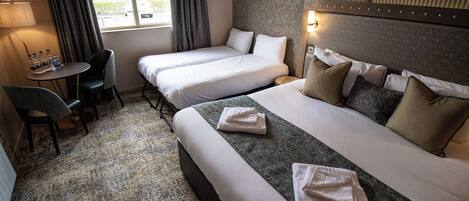 A hotel room with two beds, a small table with chairs, and a window with curtains.