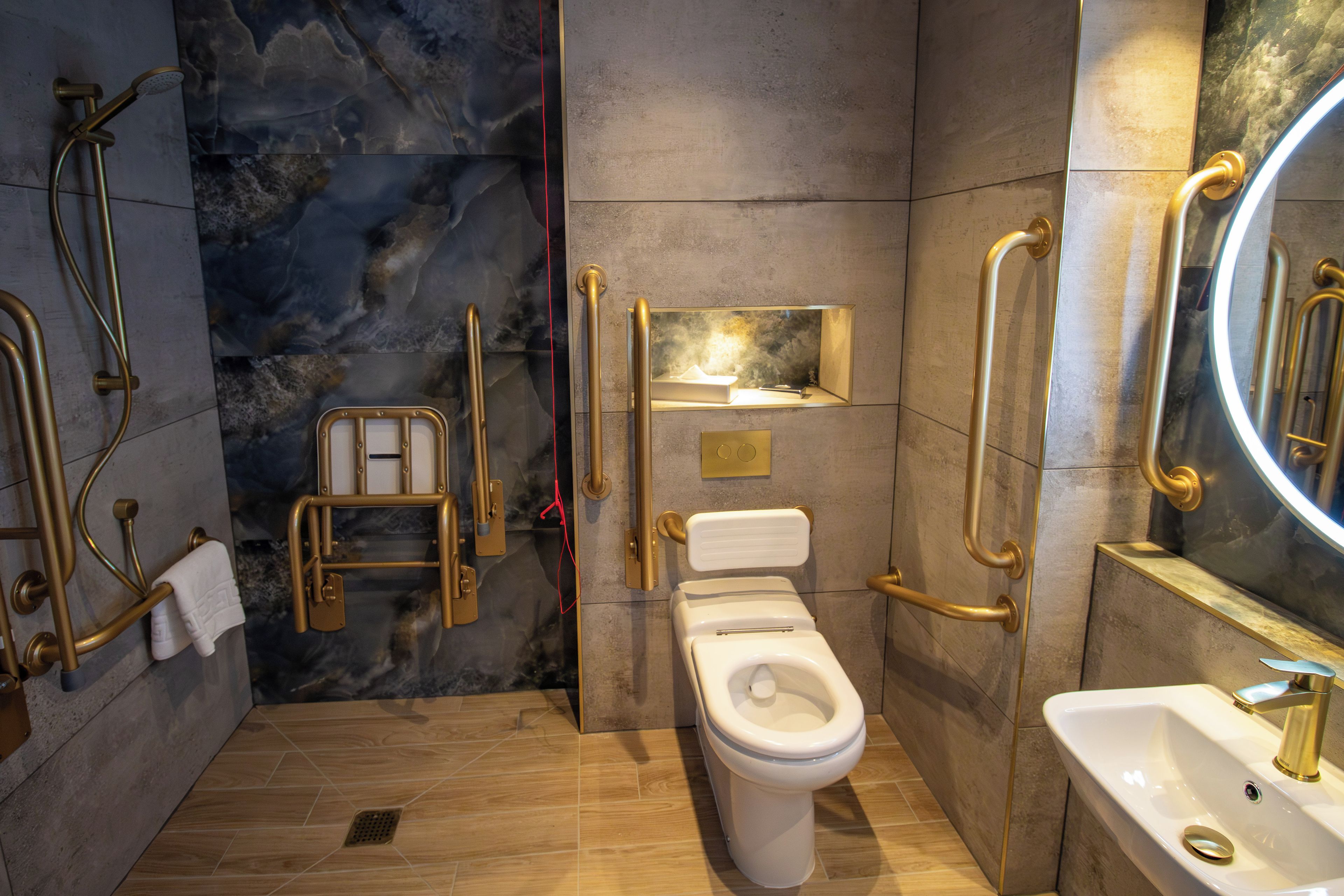A modern bathroom with a toilet, bidet, and shower area, equipped with gold-colored grab bars and a marble wall.