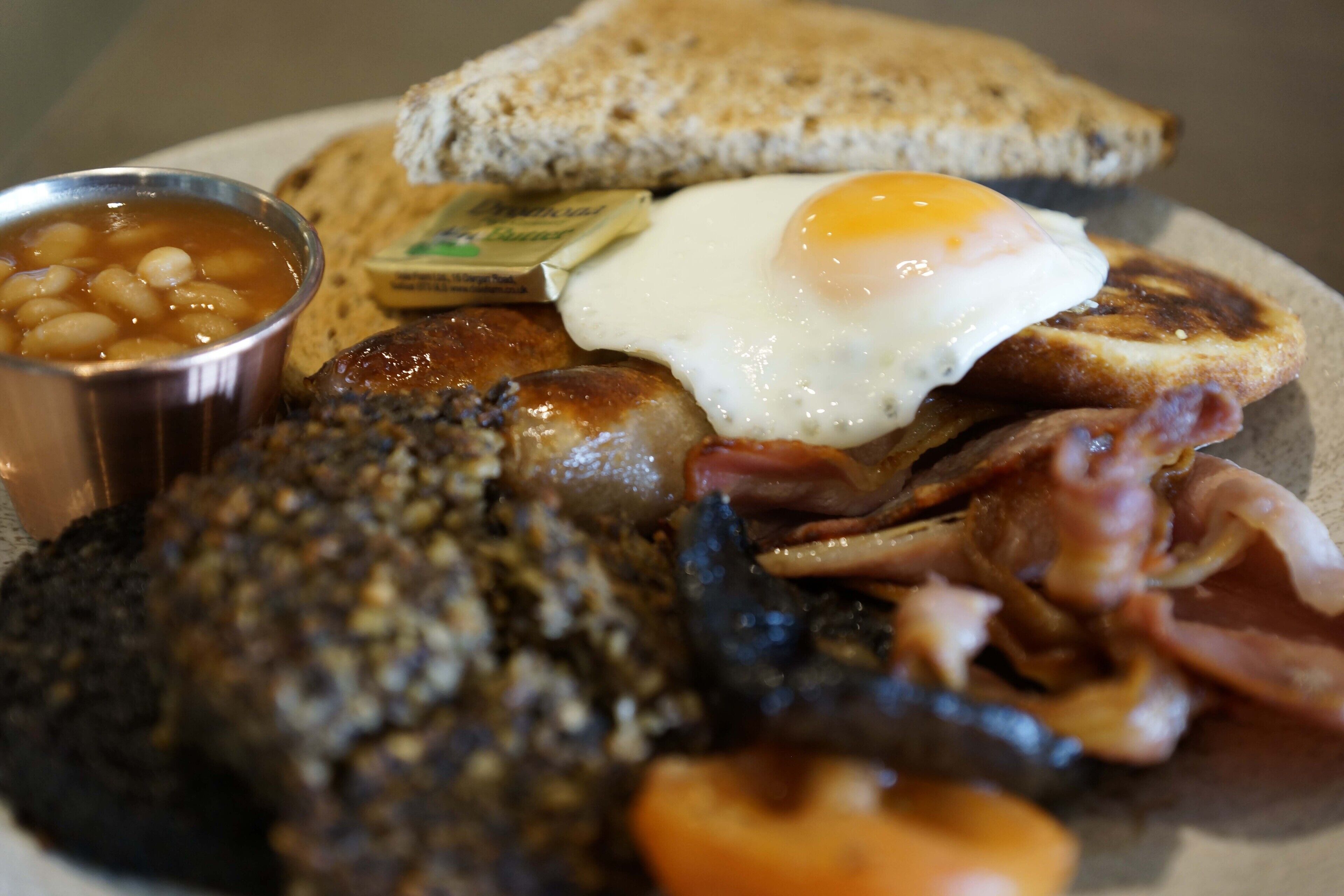 A plate of breakfast food including toast, eggs, beans, sausages, and bacon.