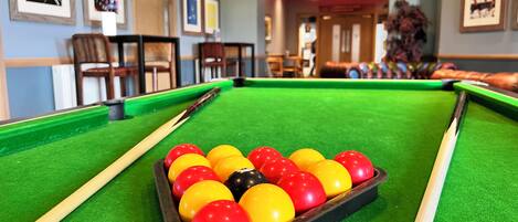 Une table de billard avec un triangle de billes disposées, dans une pièce dont les murs sont ornés de tableaux encadrés.