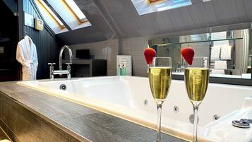Un baño moderno con una bañera grande, un tocador con espejo y dos copas de champán con fresas sobre la encimera.