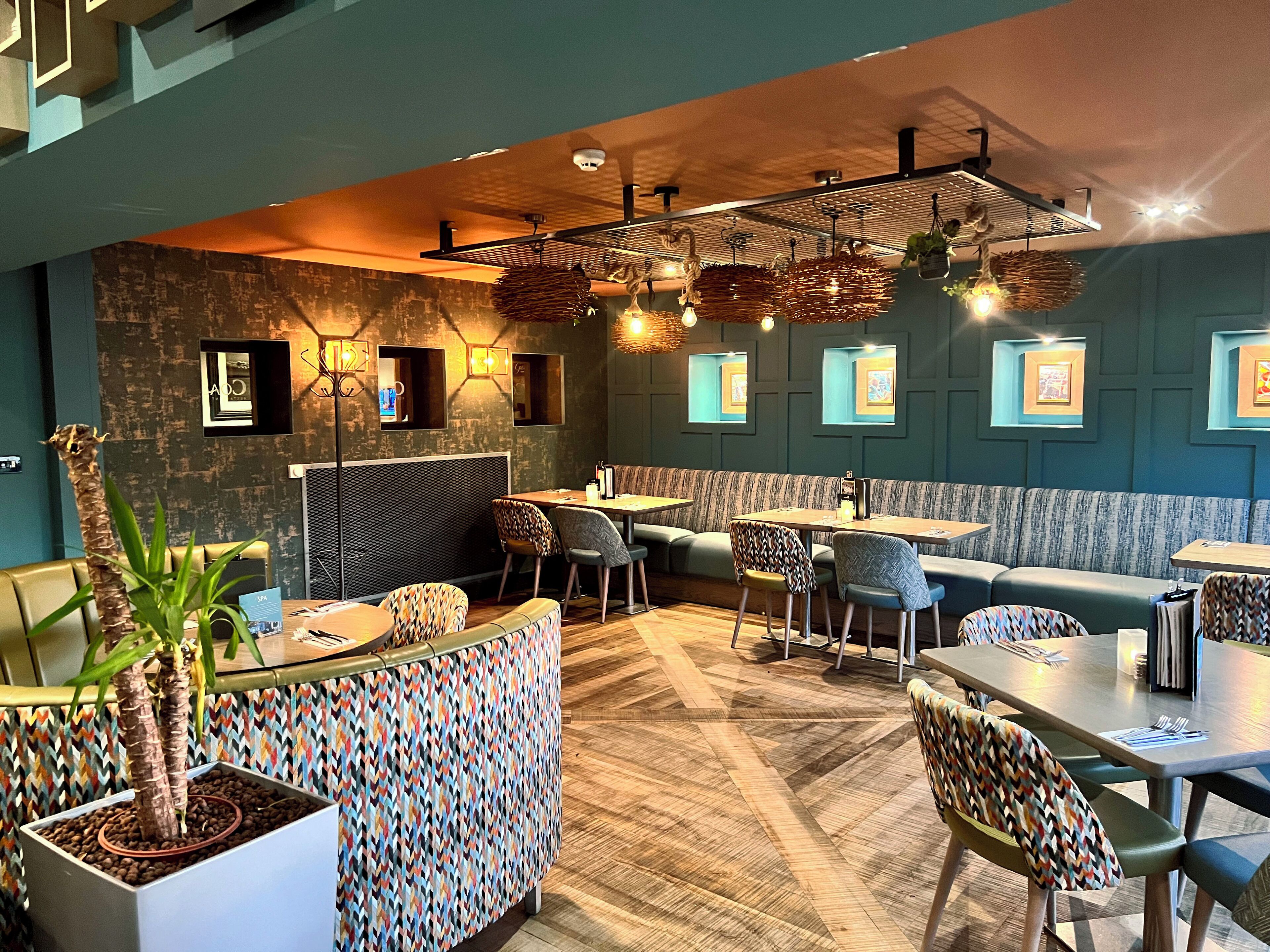 Un restaurante moderno con cabinas y mesas, cojines estampados y lámparas colgantes.