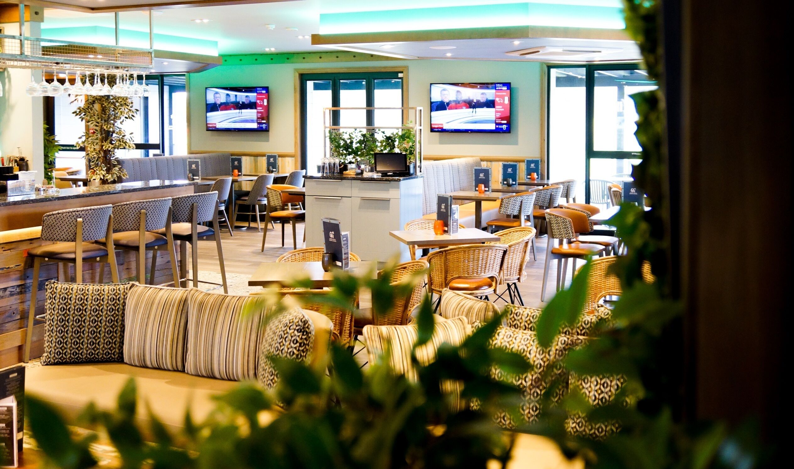 A modern hotel lobby with a bar area, seating arrangements, and two televisions mounted on the wall.