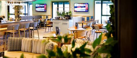 A modern hotel lobby with a bar area, seating arrangements, and two televisions mounted on the wall.