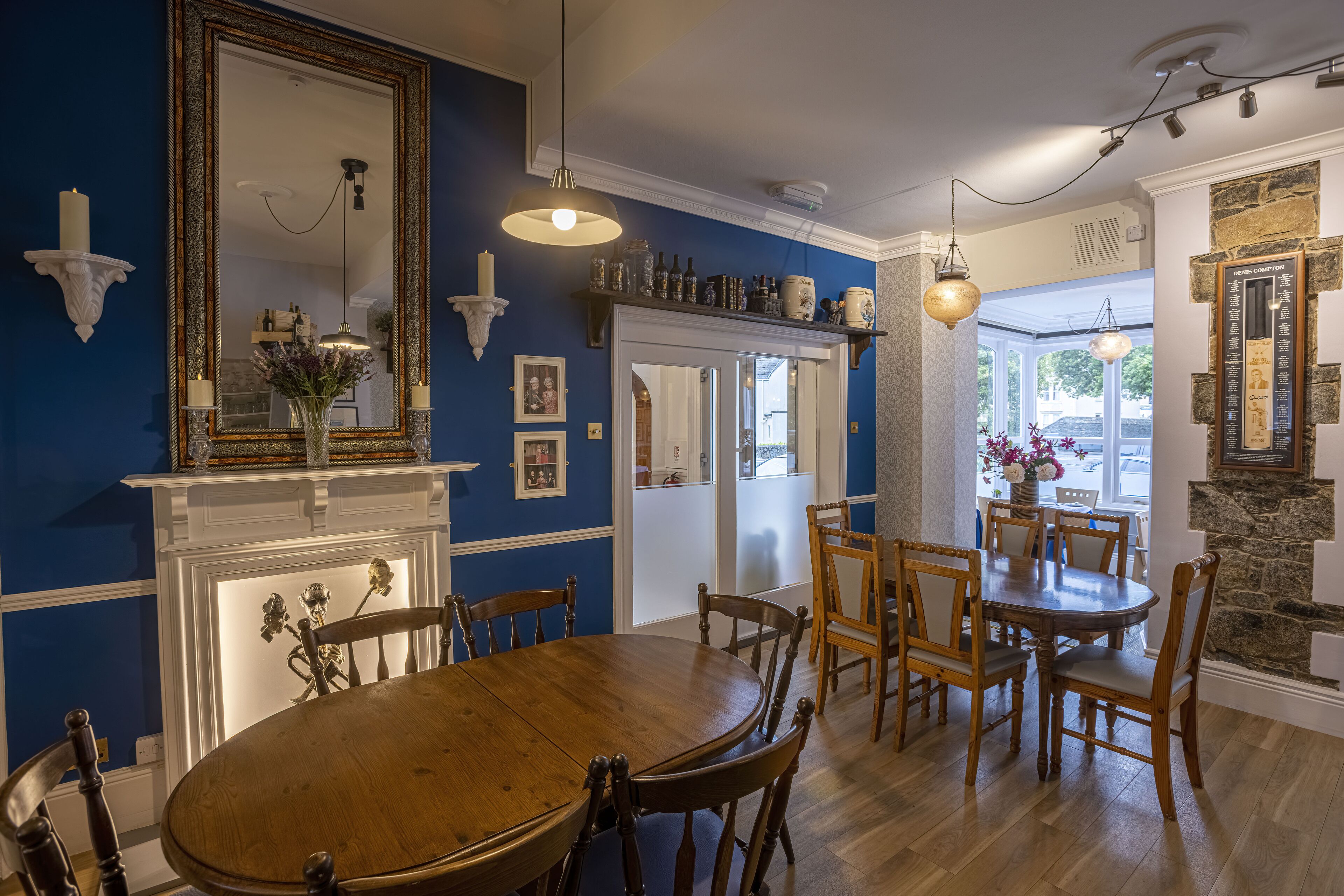 Un comedor con mesa y sillas de madera, chimenea blanca y paredes azules.