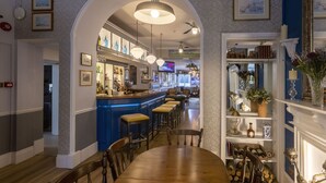 A bar area with stools, a counter, and a television screen. There is a dining area with a table and chairs, and a fireplace with decorative items. - La Collinette Hotel (St. Peter Port)