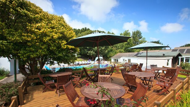 A wooden deck with outdoor furniture, including tables and chairs, and umbrellas providing shade. - La Collinette Hotel (St. Peter Port)