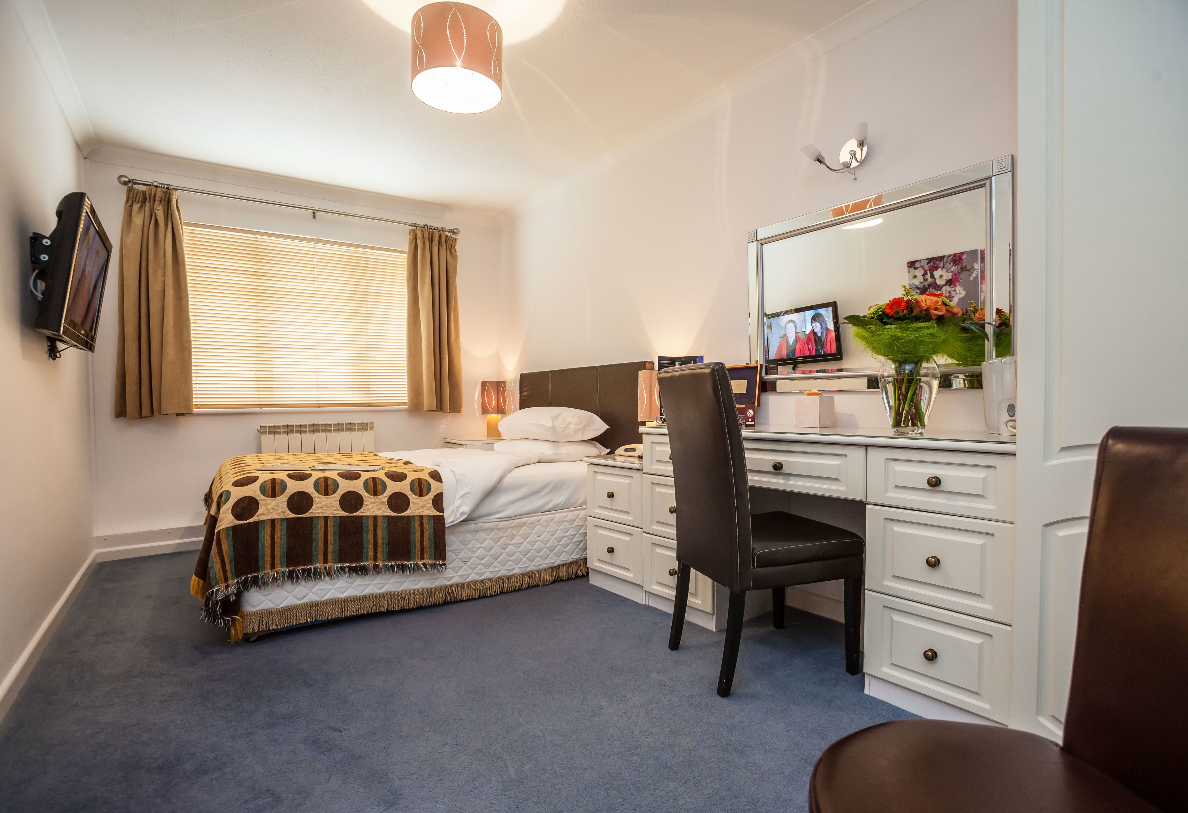 Een slaapkamer met een bed, een bureau, een stoel, een televisie en een spiegel.