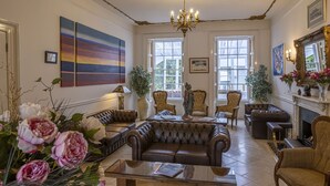 A spacious living room with a large brown leather sofa, a glass coffee table, and a fireplace. There are several armchairs and a large painting on the wall. - La Collinette Hotel (St. Peter Port)
