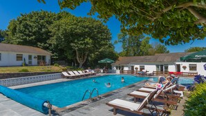 A swimming pool with lounge chairs and umbrellas, surrounded by trees and buildings. - La Collinette Hotel (St. Peter Port)