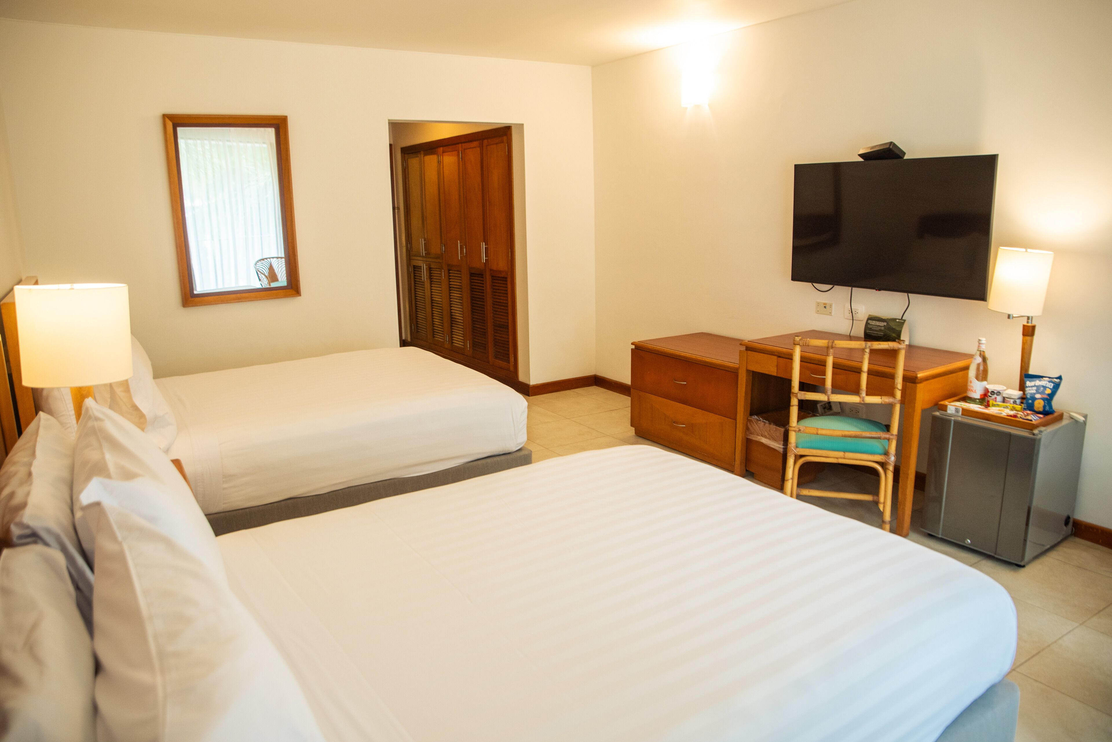 Une chambre d’hôtel avec deux lits, un bureau avec une chaise, une télévision et un petit placard.