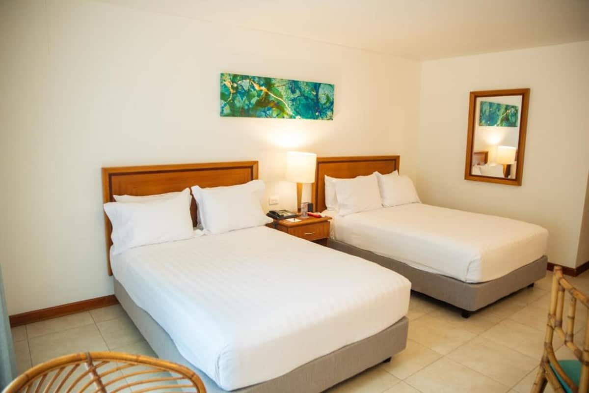 A hotel room with two single beds, a wooden headboard, a nightstand with a lamp, a mirror, and a wall painting.