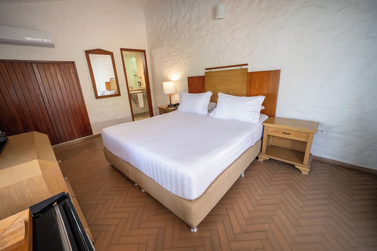 A hotel room with a large bed, wooden wardrobe, bedside table, and a mirror.
