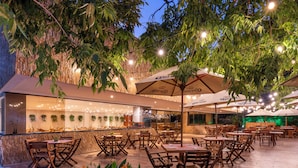 Un área de comedor al aire libre con mesas, sillas, luces colgantes y sombrillas.