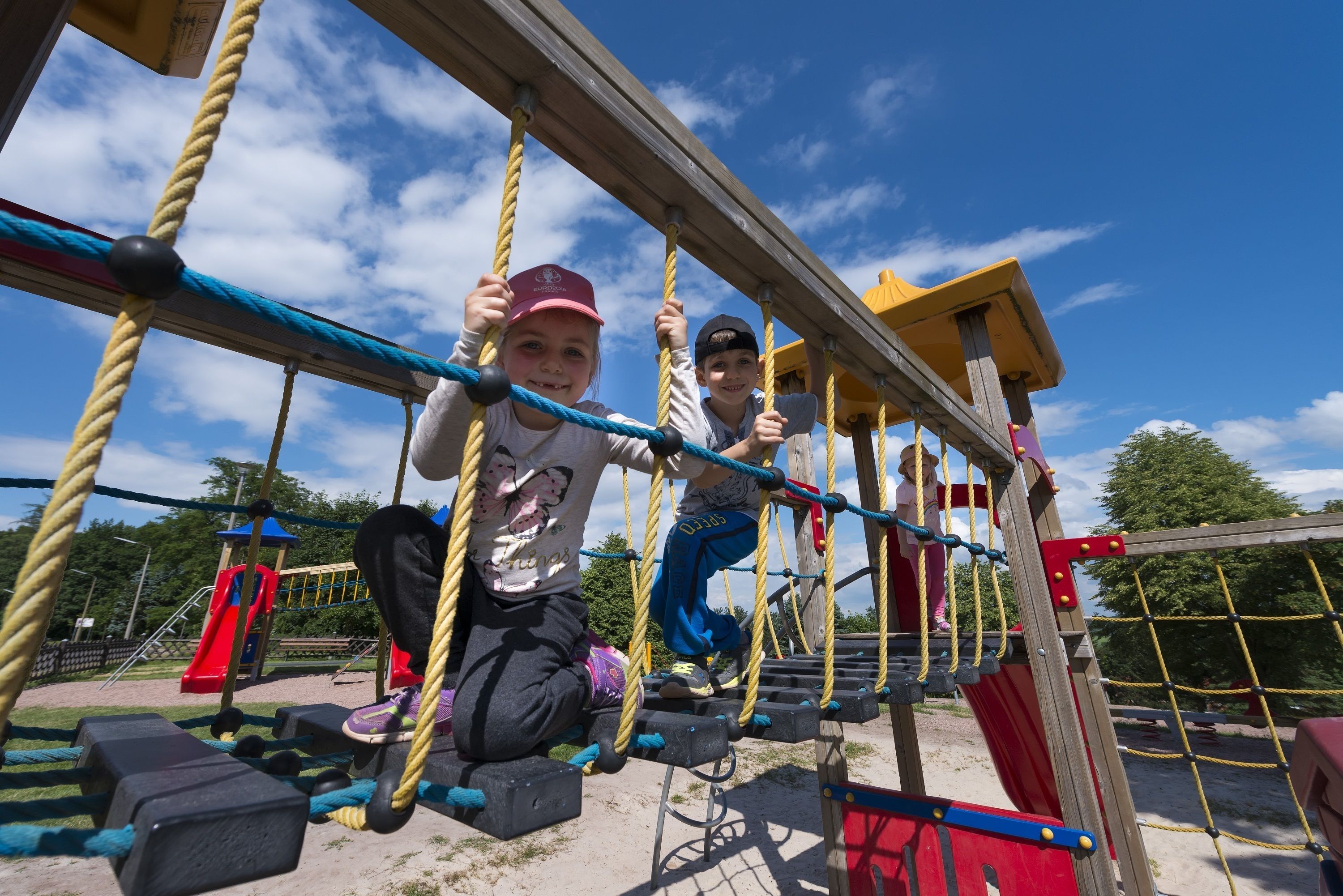 Children playing on a rope bridge at a playground.