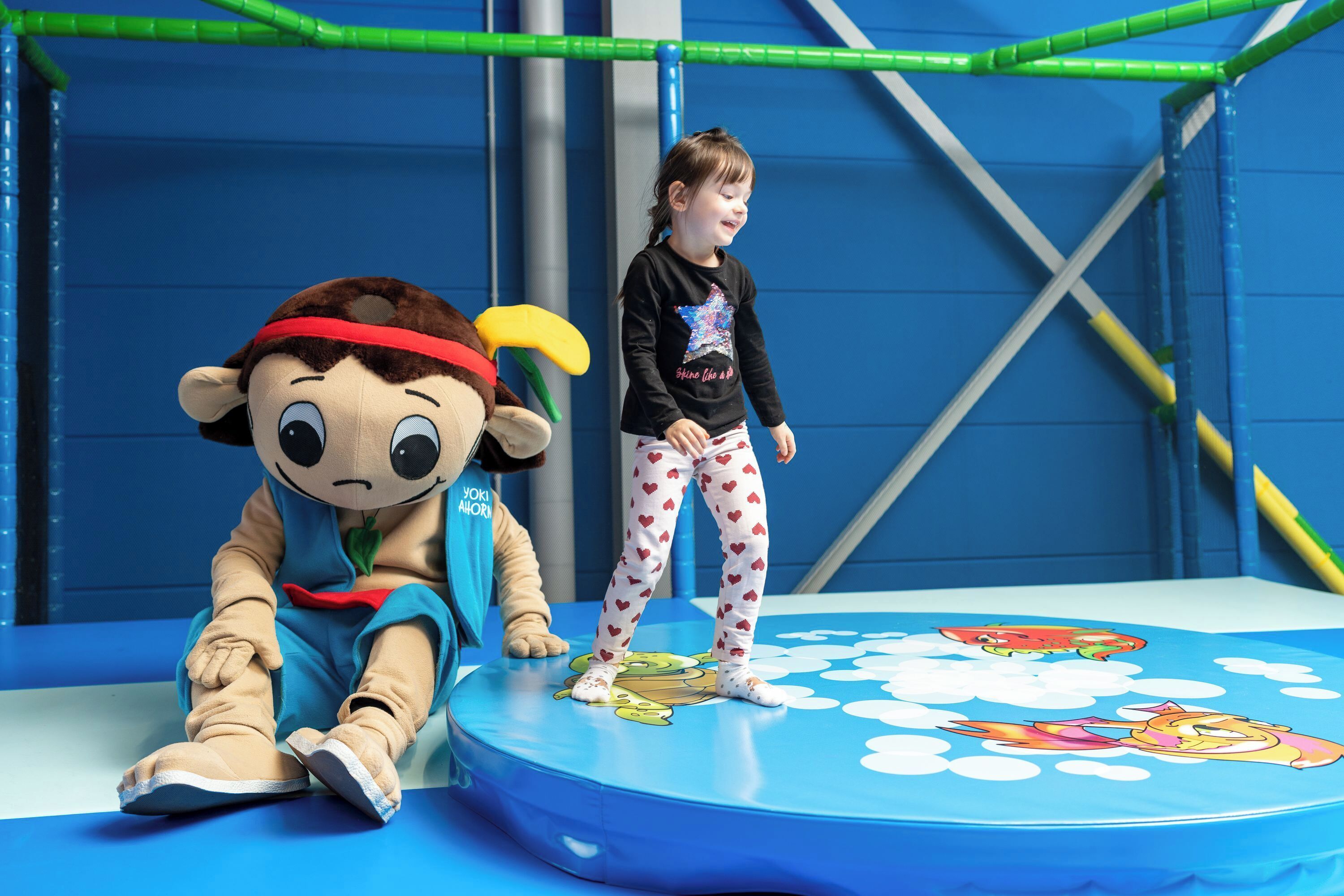 A child playing on a blue play area with cartoon characters, a plush toy, and a climbing structure.