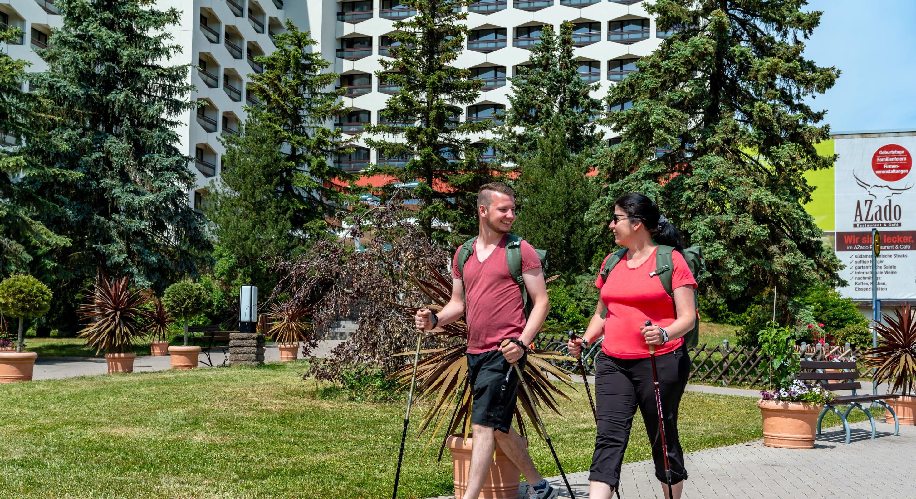 Two people walking in a park with potted plants and a building in the background.