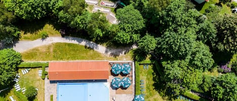 An aerial view of a resort with a swimming pool, sun loungers, and a red-roofed building.