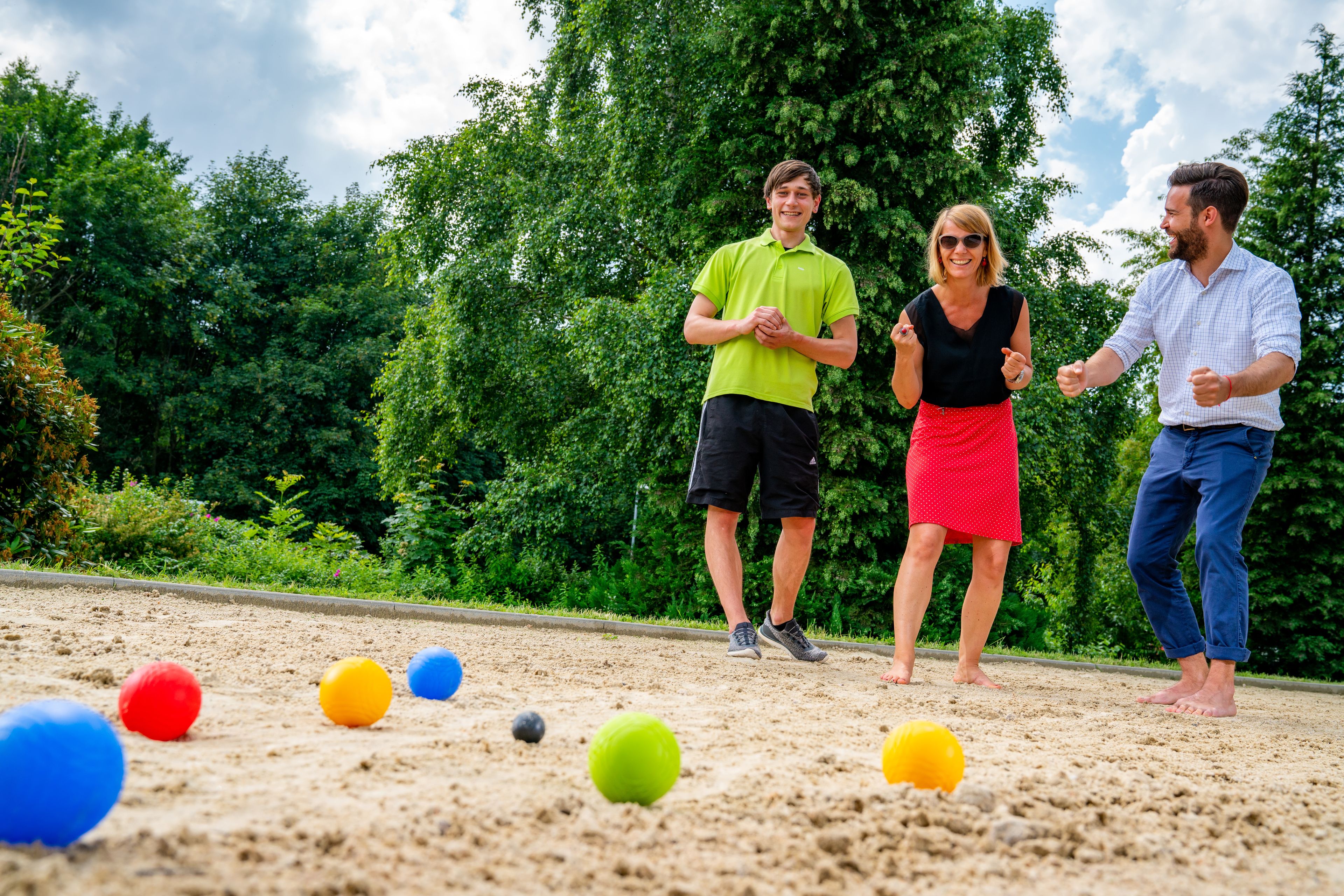 Three people playing a game with colorful balls on a sandy surface.
